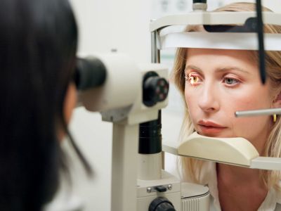 Donna, optometria e lampada a fessura con apparecchio, valutazione della vista o cura della salute oculare in clinica. Persona, controllo e paziente per la salute, luce e laser per scansione della retina con lente per esame dell’occhio.