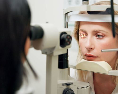 Donna, optometria e lampada a fessura con apparecchio, valutazione della vista o cura della salute oculare in clinica. Persona, controllo e paziente per la salute, luce e laser per scansione della retina con lente per esame dell’occhio.